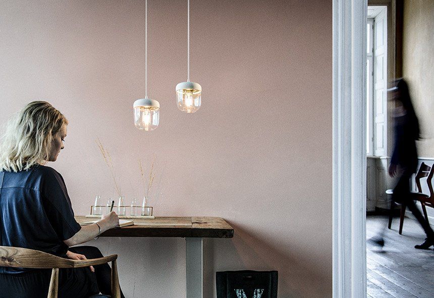 A woman is sitting at a table in a room with a pink wall.