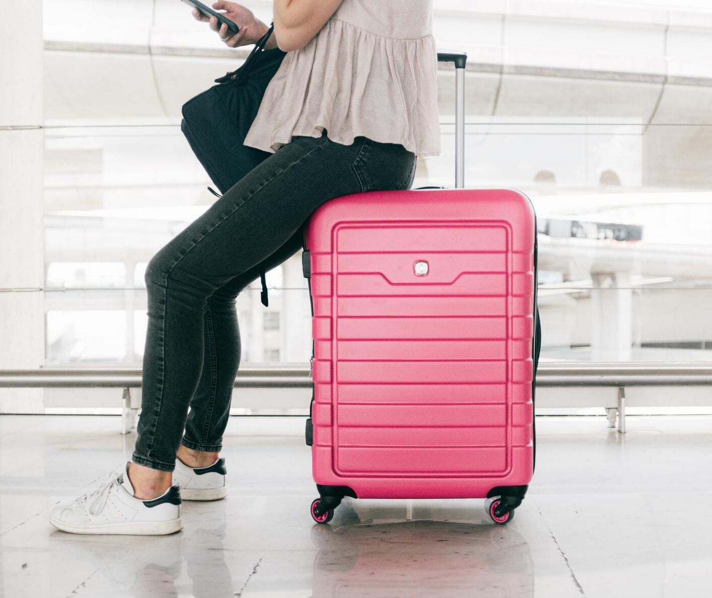 Femme assise sur une valise rose dans un aéroport