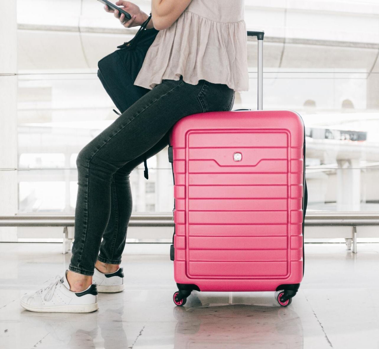 Frau sitzt auf einem rosafarbenen Koffer in einem Flughafen