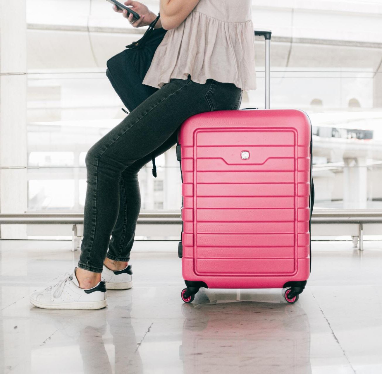 Woman sitting on a pink suitcase in an airport