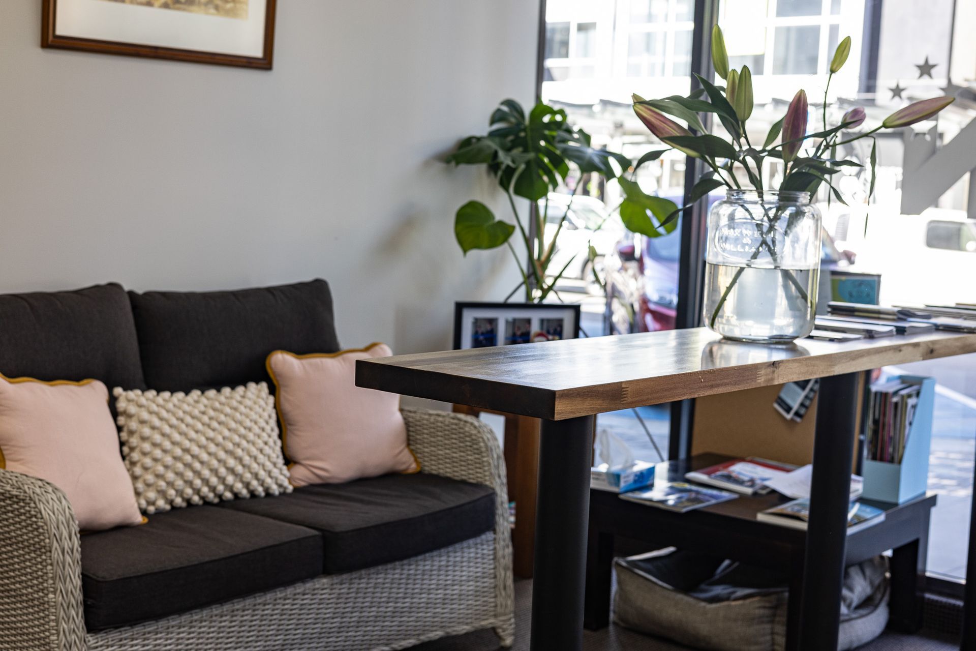 A waiting area with a dark sofa, table with greenery, and a bright window view.