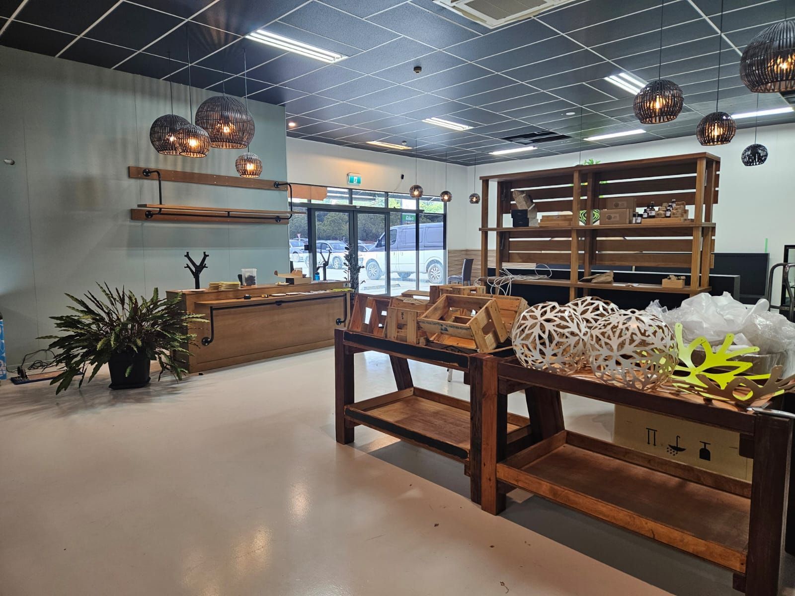Empty retail space with wooden shelves, displays, and decorative pendant lights. Light gray floor, muted color walls.