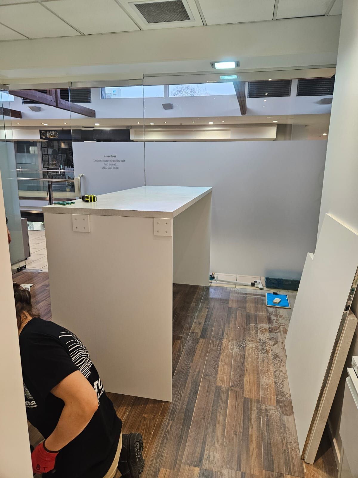 Person installing a white counter and wall in a commercial space with wooden flooring.