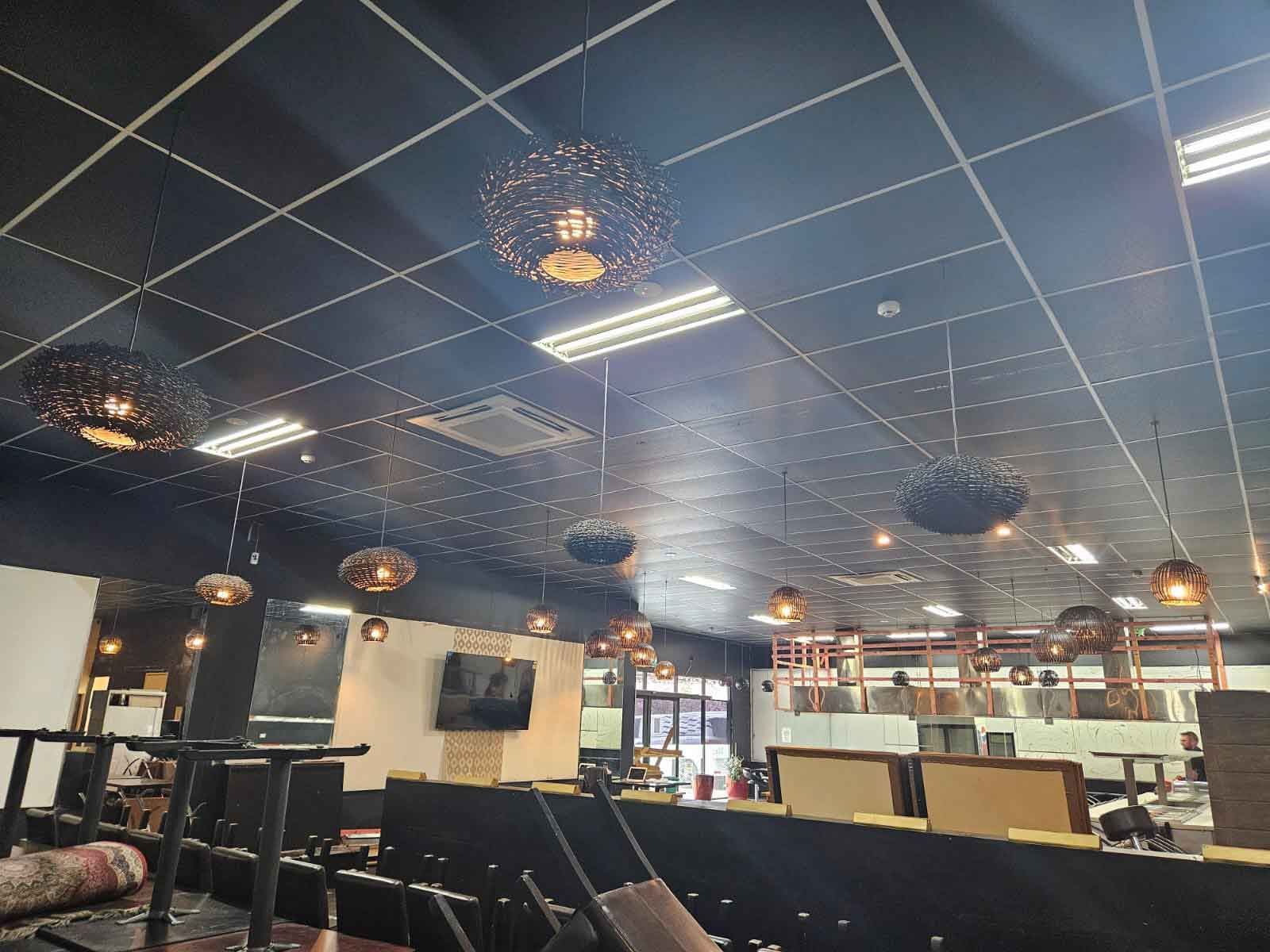 Restaurant interior with black ceiling, pendant lights, tables and bar.