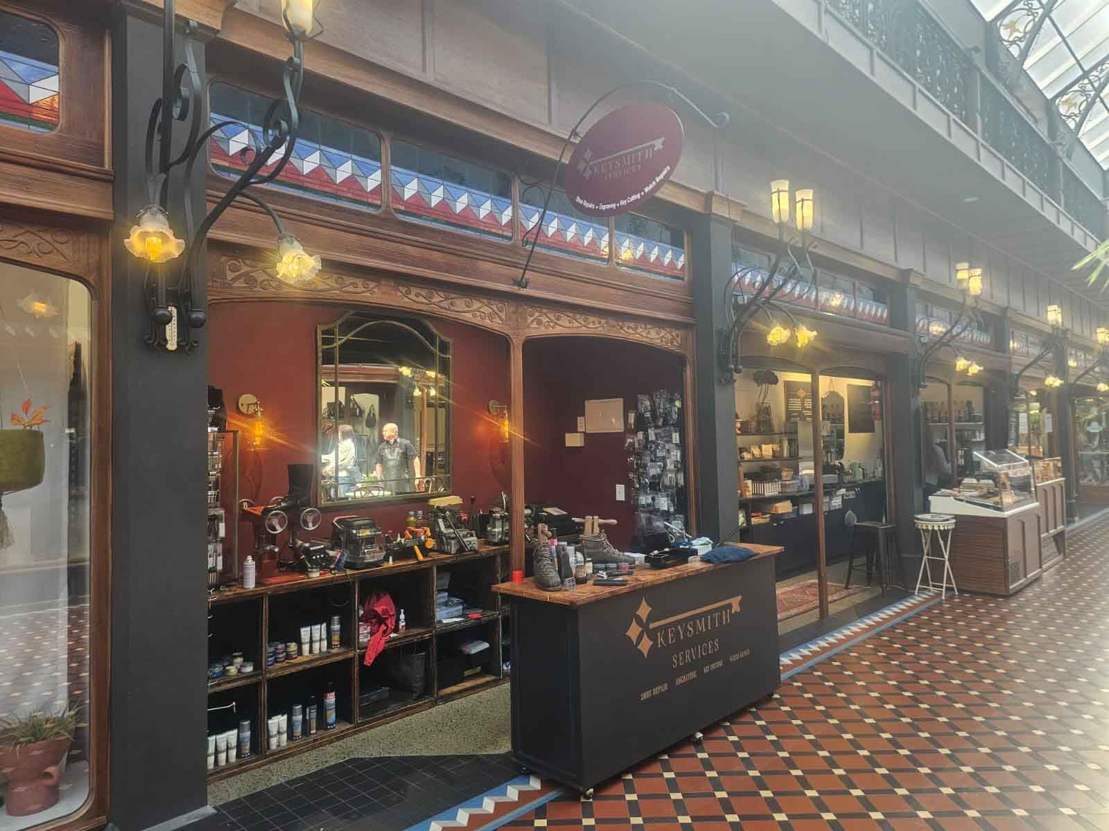 Shops in an arcade with tile floor, black storefronts, and decorative ironwork; sign above says