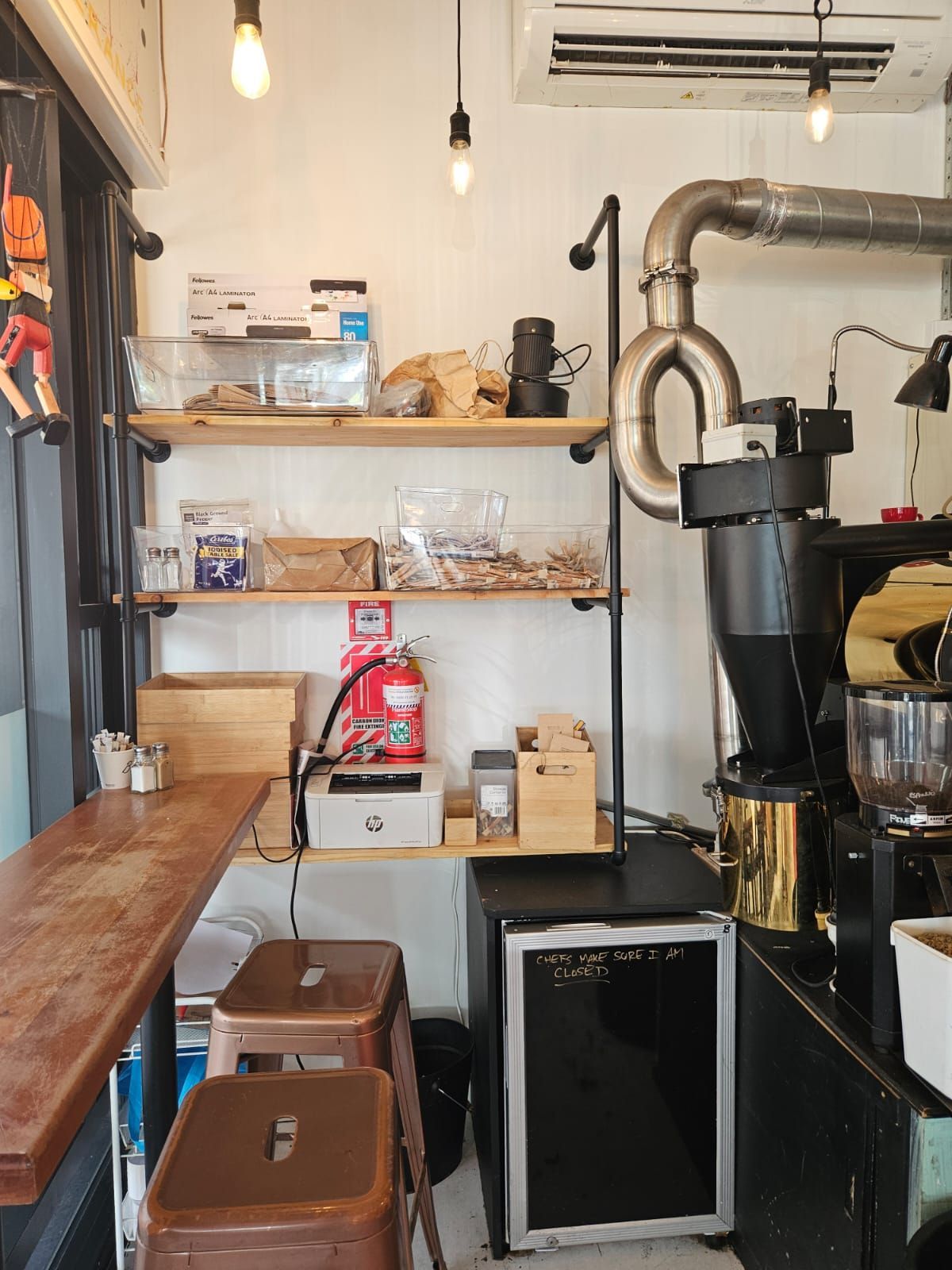 Coffee shop interior: shelving with coffee beans, equipment, wooden counter, and stools.