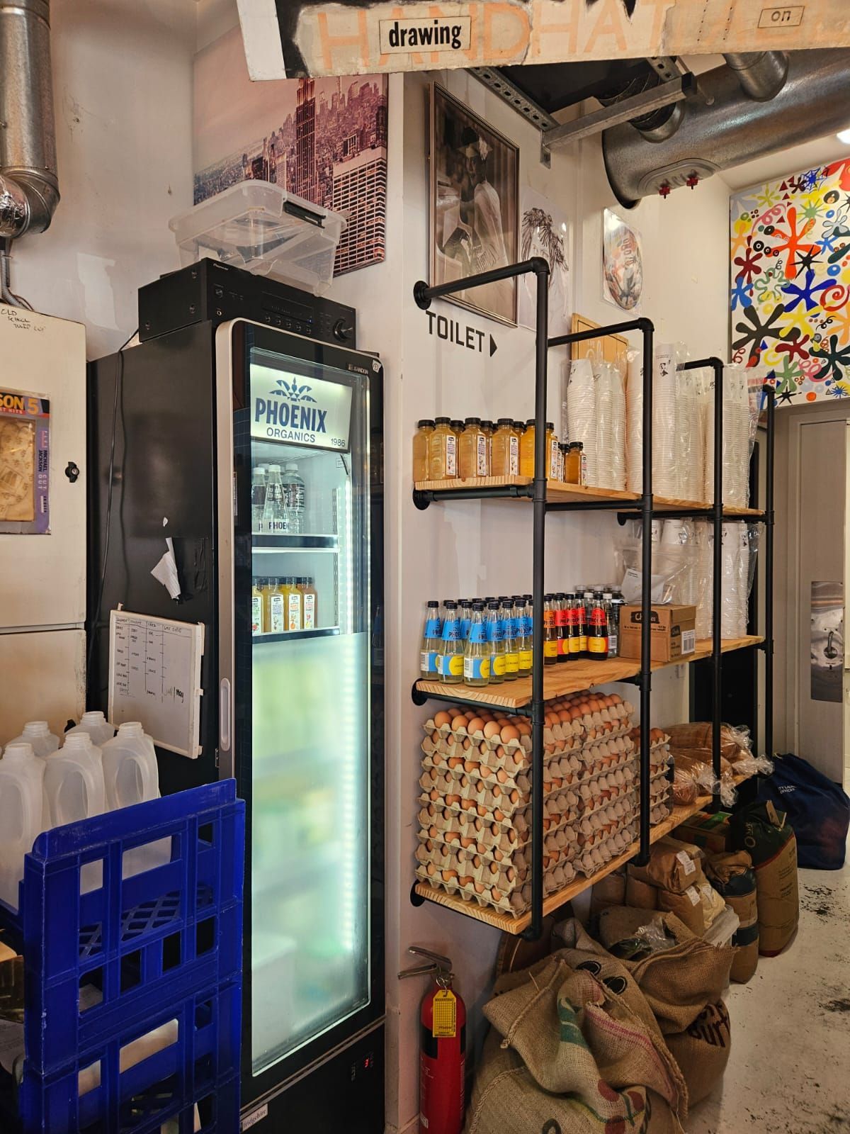 Cafe interior: refrigerator, shelves with jars, eggs, and sacks of goods.