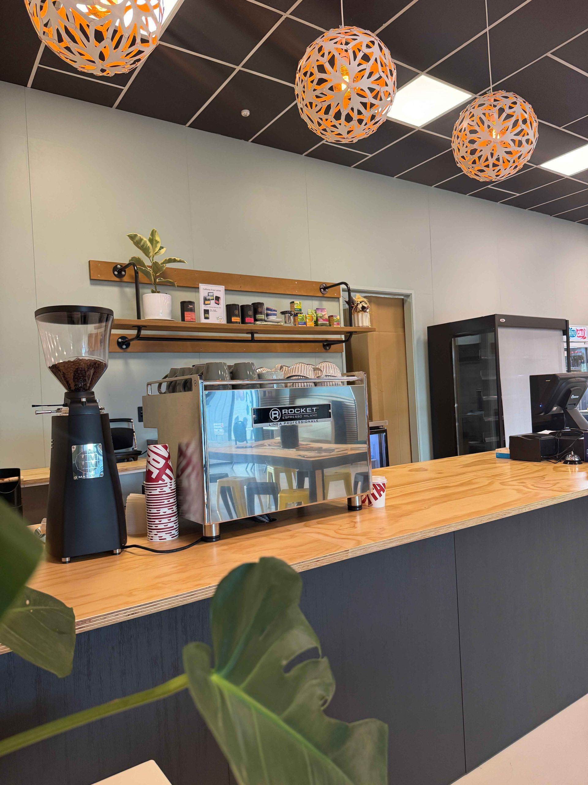 Coffee shop counter with espresso machine, grinder, and decorative hanging lights.