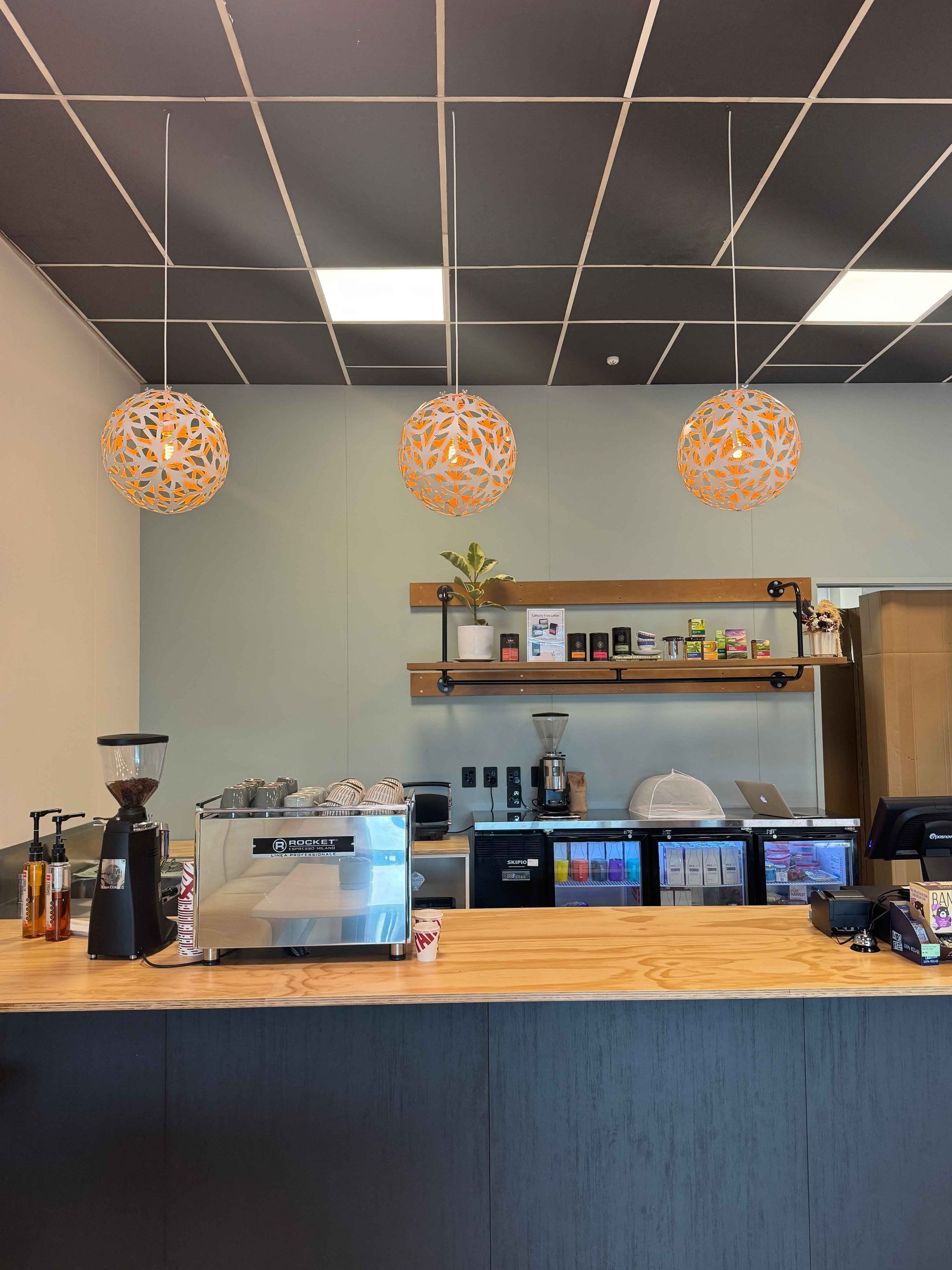 Coffee shop counter with espresso machine, grinders, and hanging globe lights.