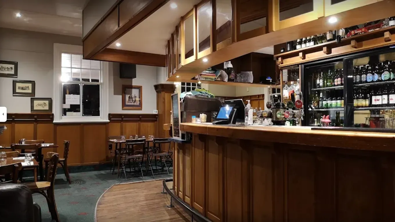 Wooden bar interior with tables, stools, and bar supplies, a warm, inviting atmosphere.