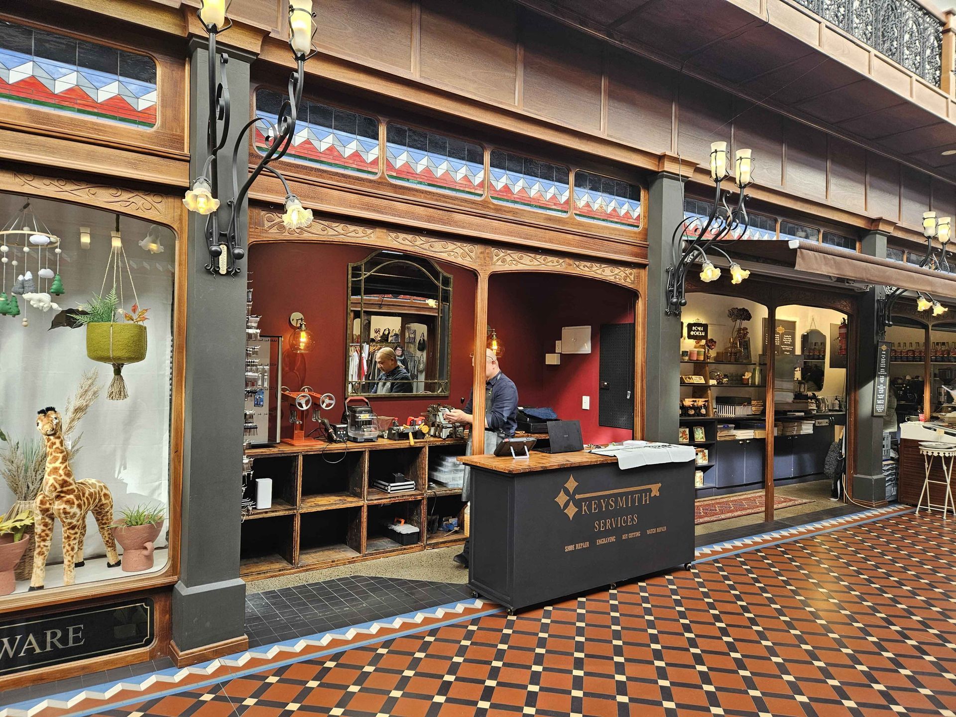Shops inside a red and brown tiled shopping arcade. A person stands behind a black counter in the center.