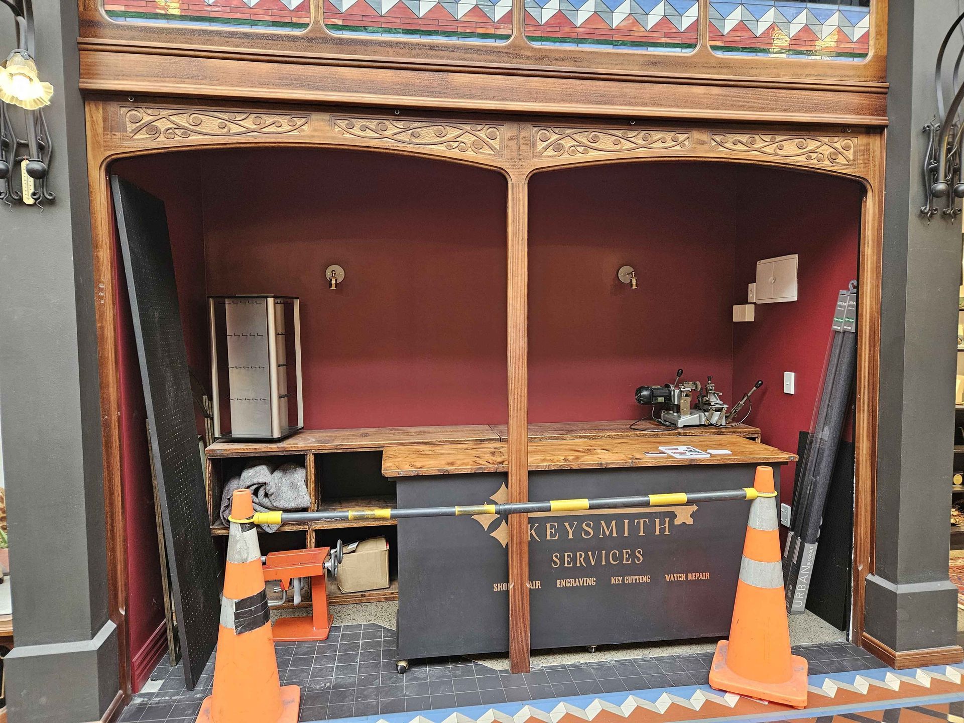 A weathered bar interior with a fridge, counter, and safety cones. Red walls and ornate wood trim.