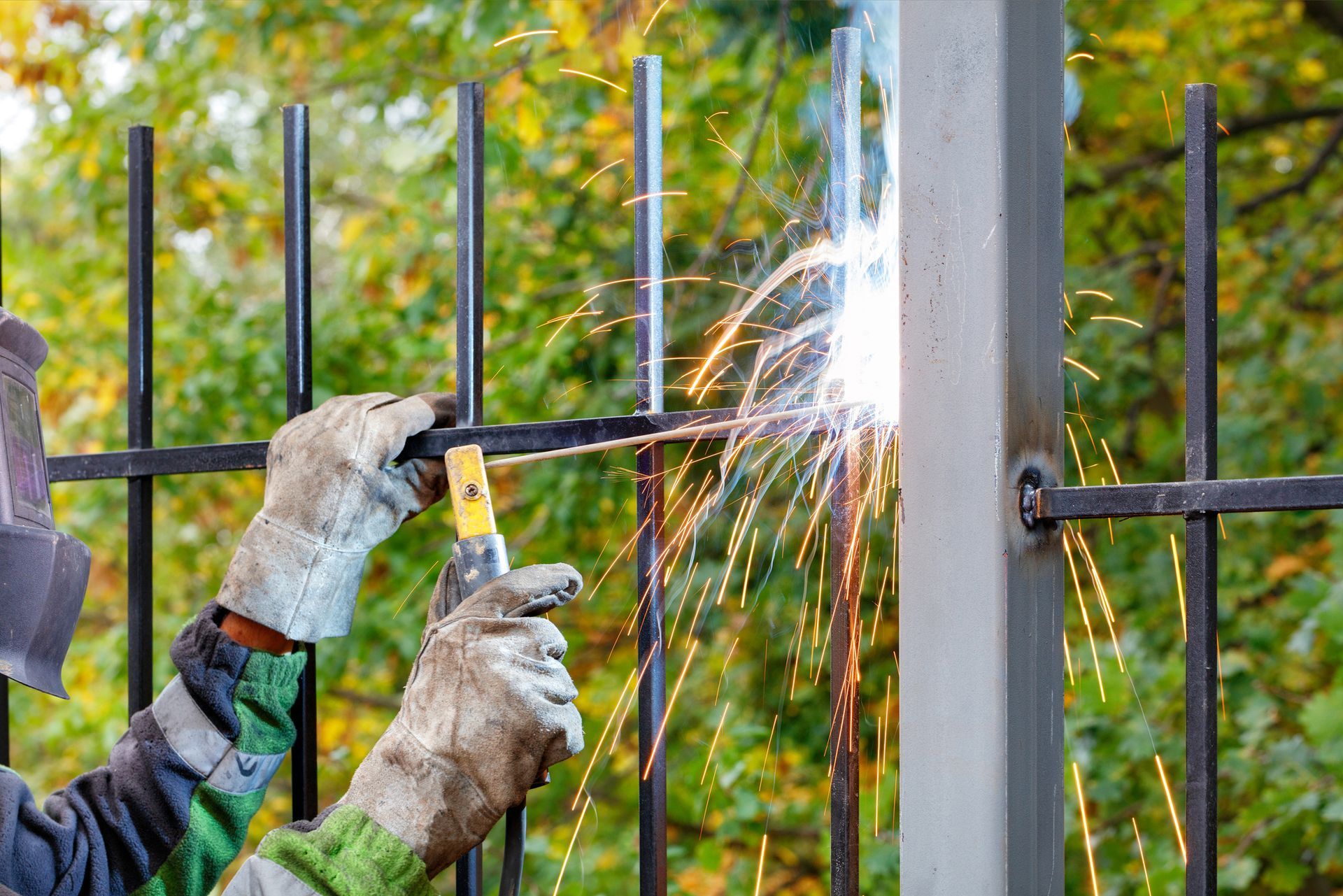 A man is welding a metal fence with a welding machine.