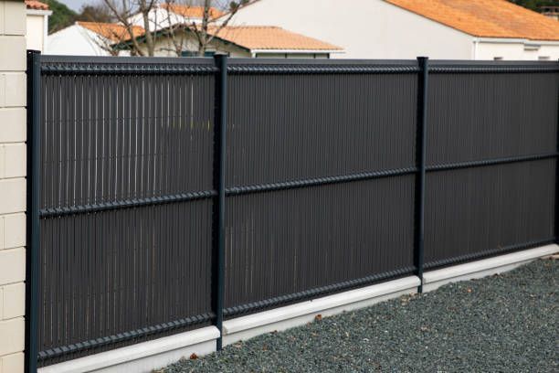 A black fence is surrounded by gravel in front of a house.