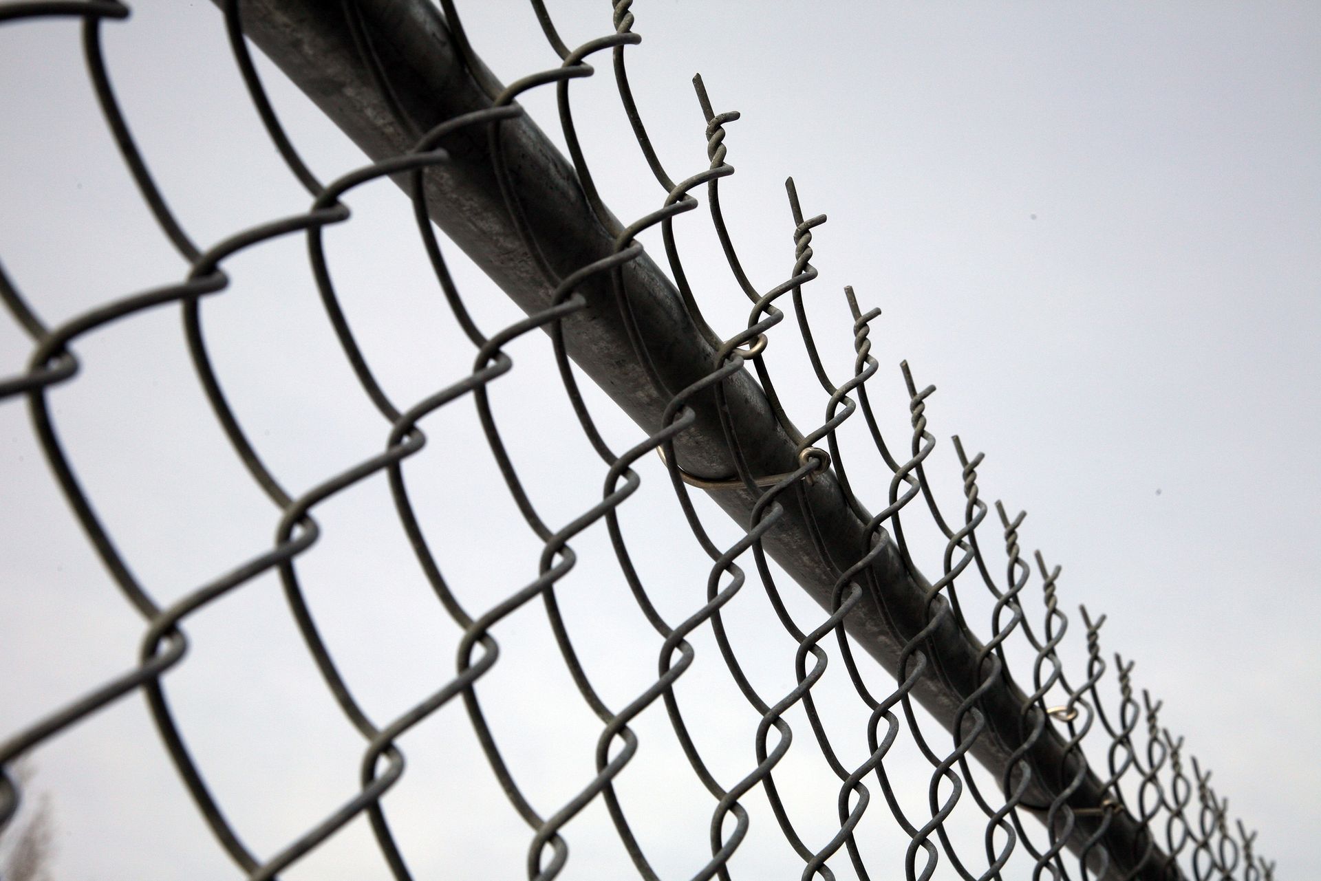 A chain link fence is against a white sky.