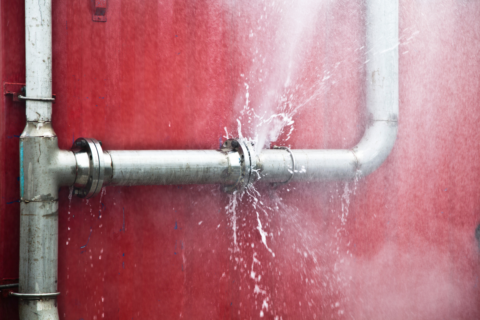 A pipe is leaking water on a red wall.