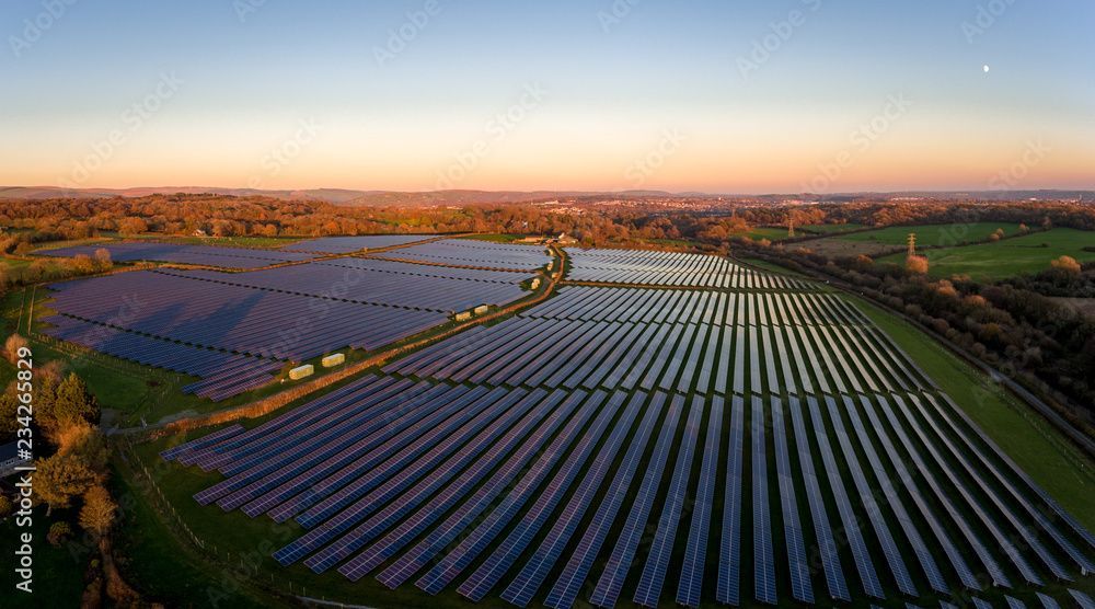 Aerial view of rows of solar panels in a field at sunset under a clear sky.