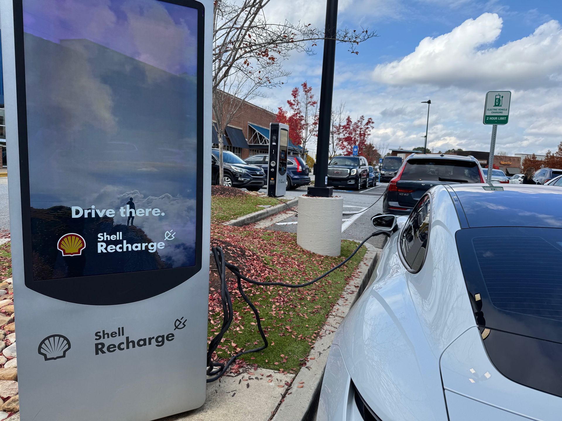 Electric car charging at a Shell Recharge station in a parking lot.