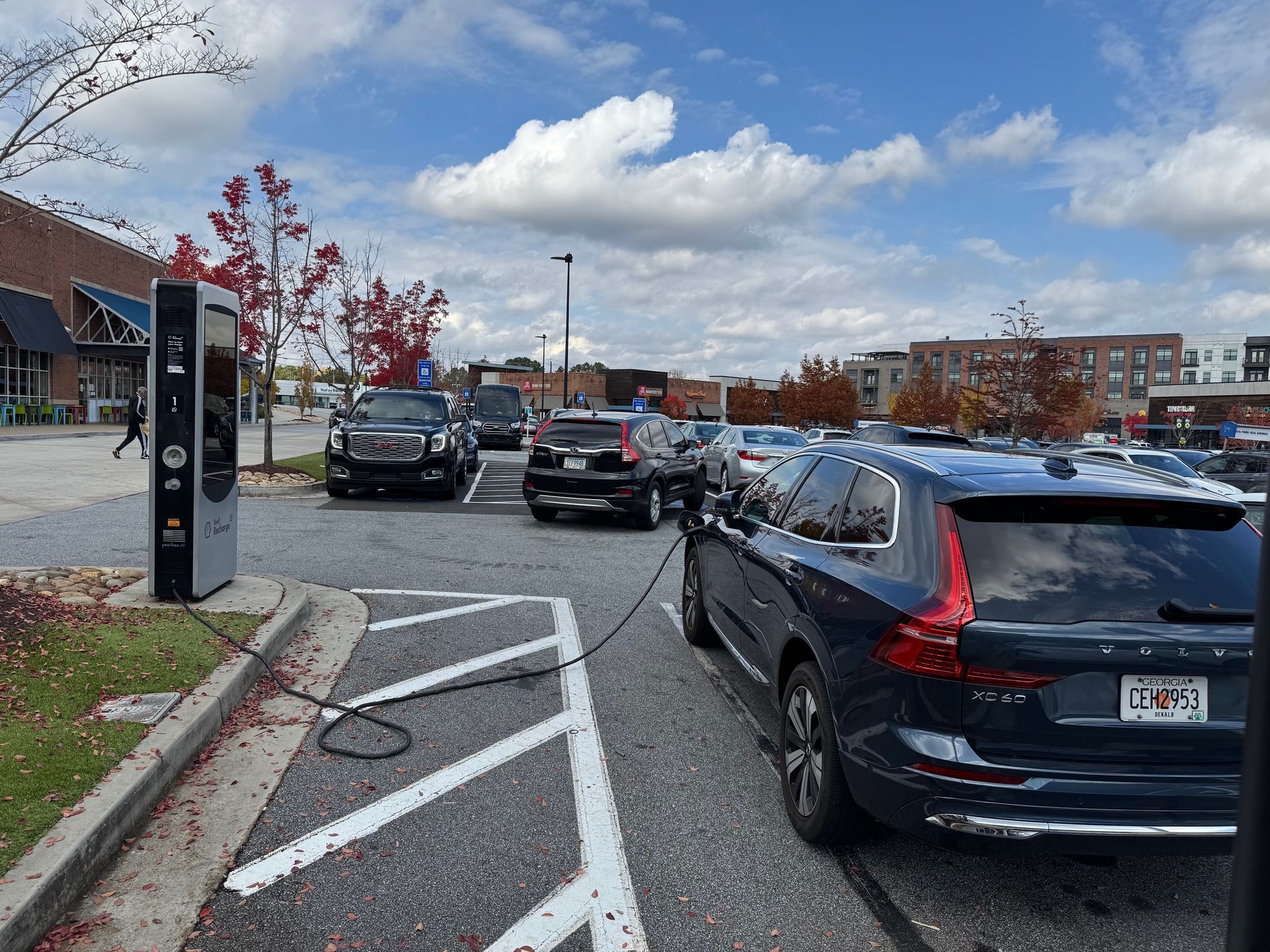 Electric vehicles charging at a station in a parking lot on a sunny day.