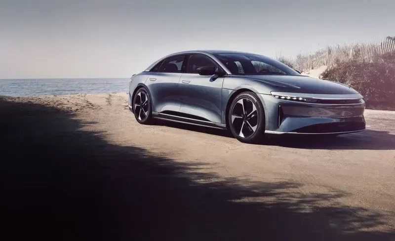 Silver Lucid Air electric sedan parked on a sandy beach road next to the ocean.