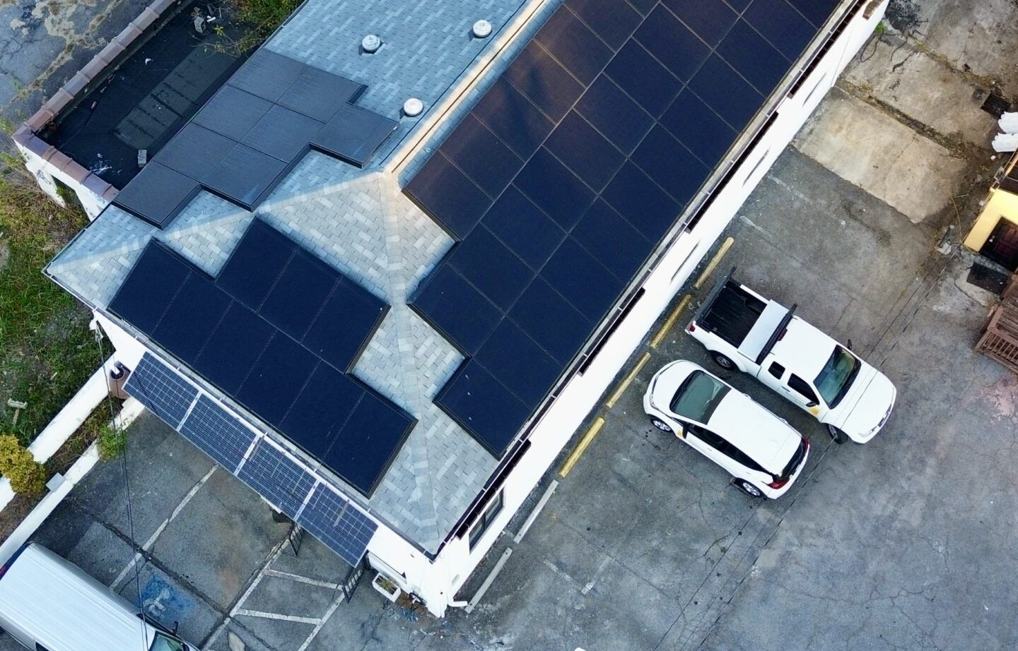 Solar panels on a building roof, next to parked white vehicles.