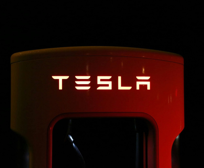 Illuminated Tesla Supercharger station with white logo against a dark background.