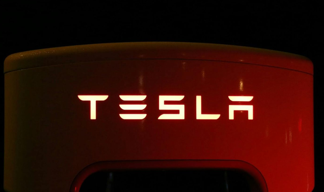 Illuminated Tesla logo on a charging station, glowing white against a dark backdrop.