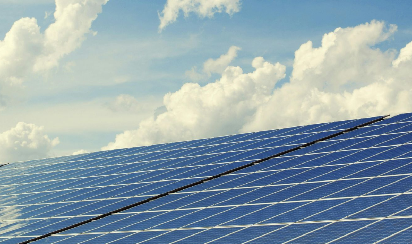 Solar panels against a blue sky with fluffy white clouds.