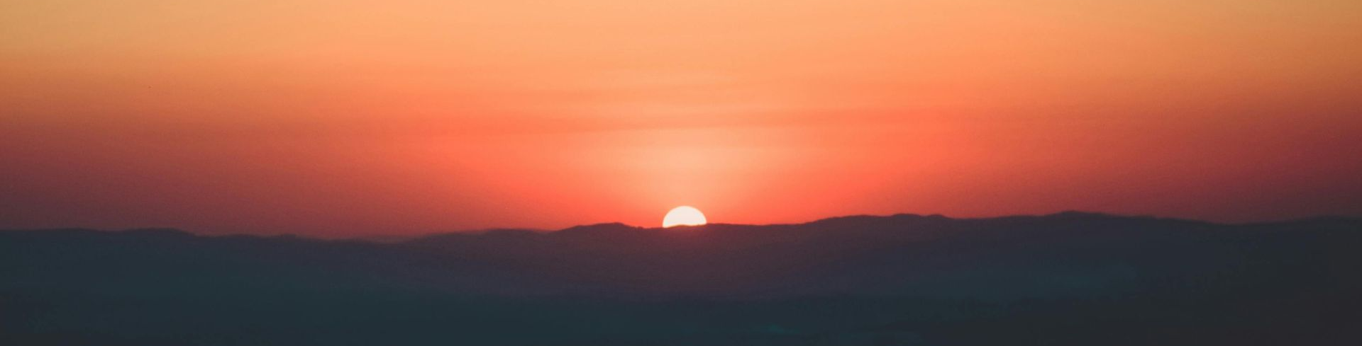 Sunset over a hazy horizon, with shades of orange and red in the sky.