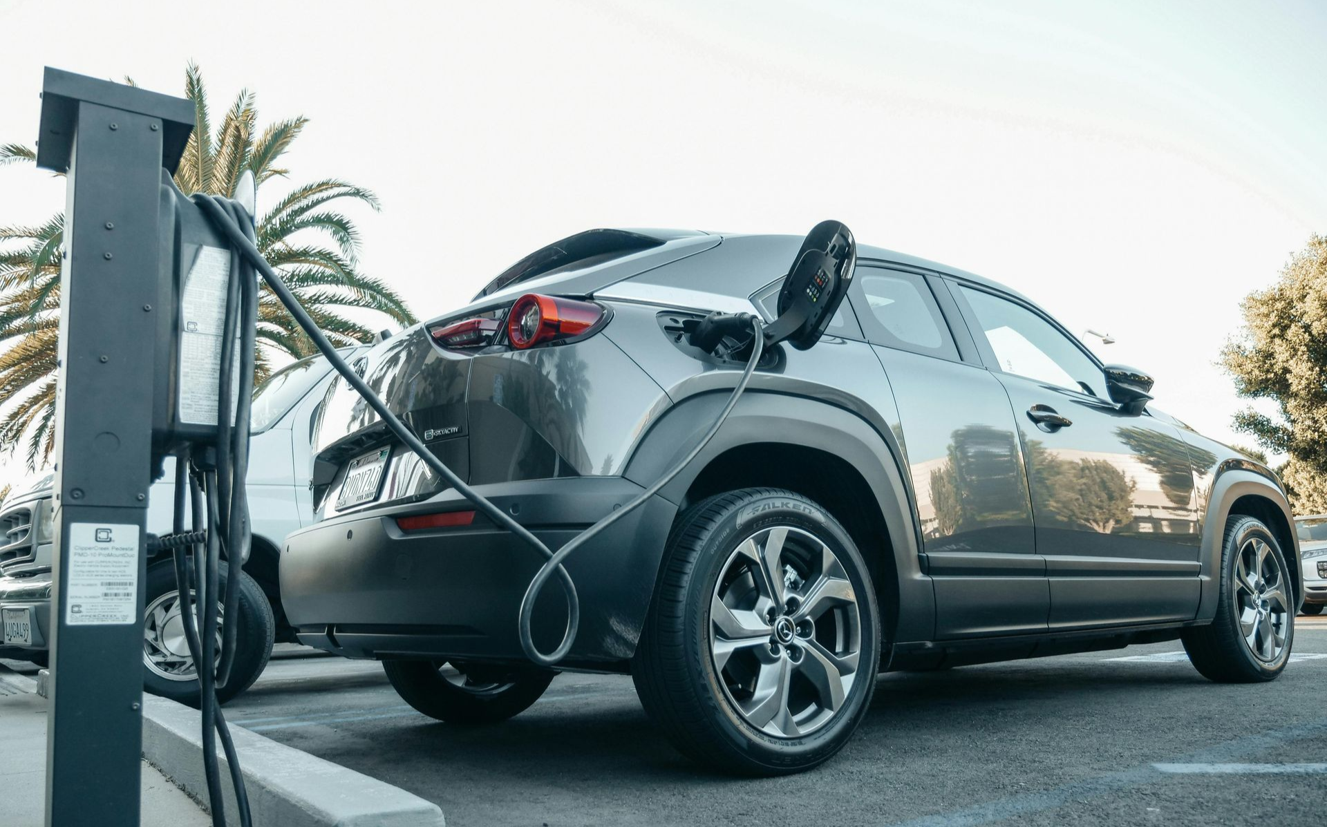 A dark gray electric SUV parked at a charging station, with a charging cable plugged into its rear port.