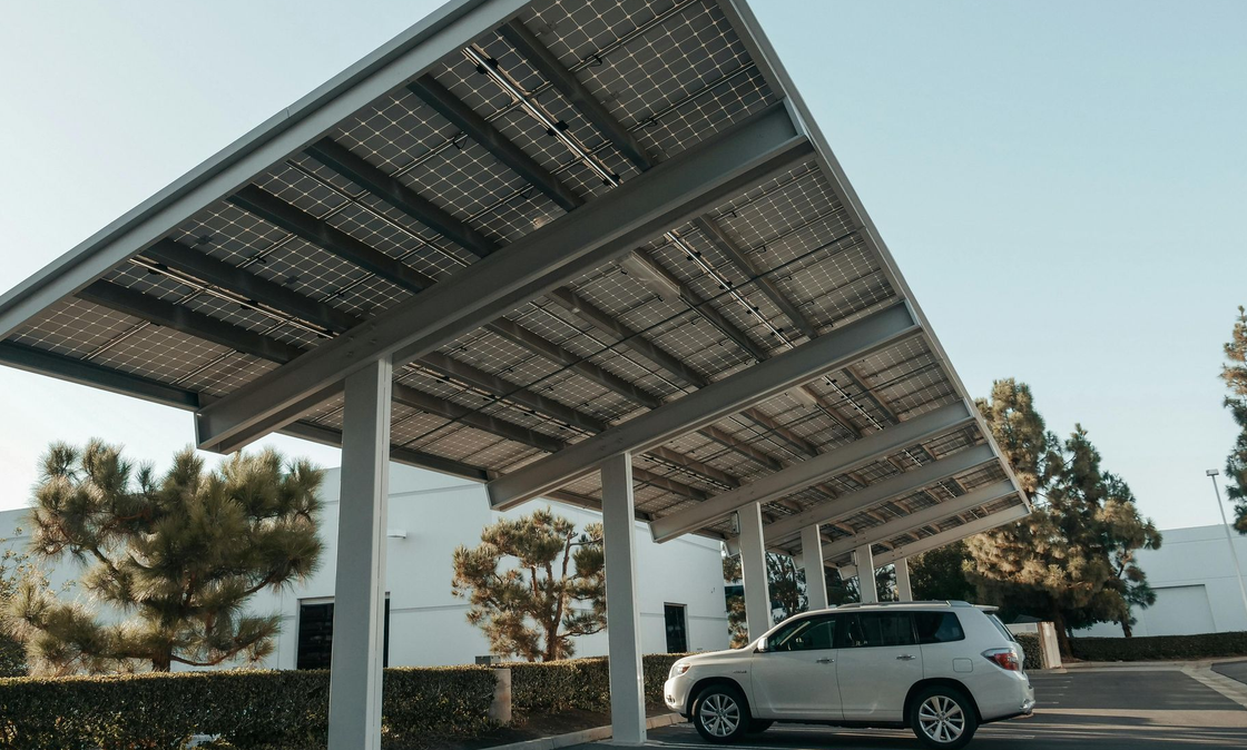 White SUV parked under solar panel canopy in parking lot.