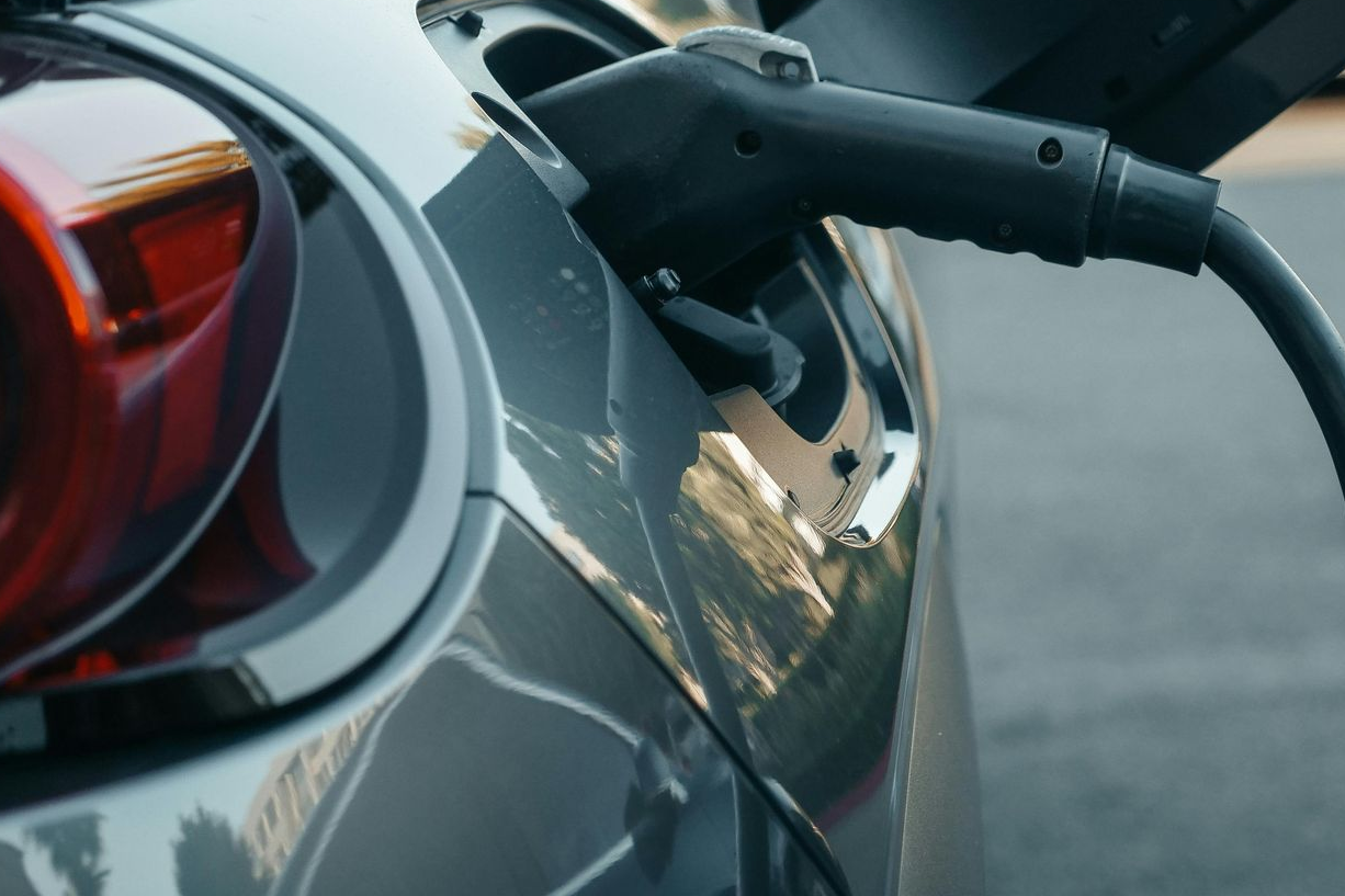 Electric car charging: cable plugged into port on gray vehicle, red taillight visible.