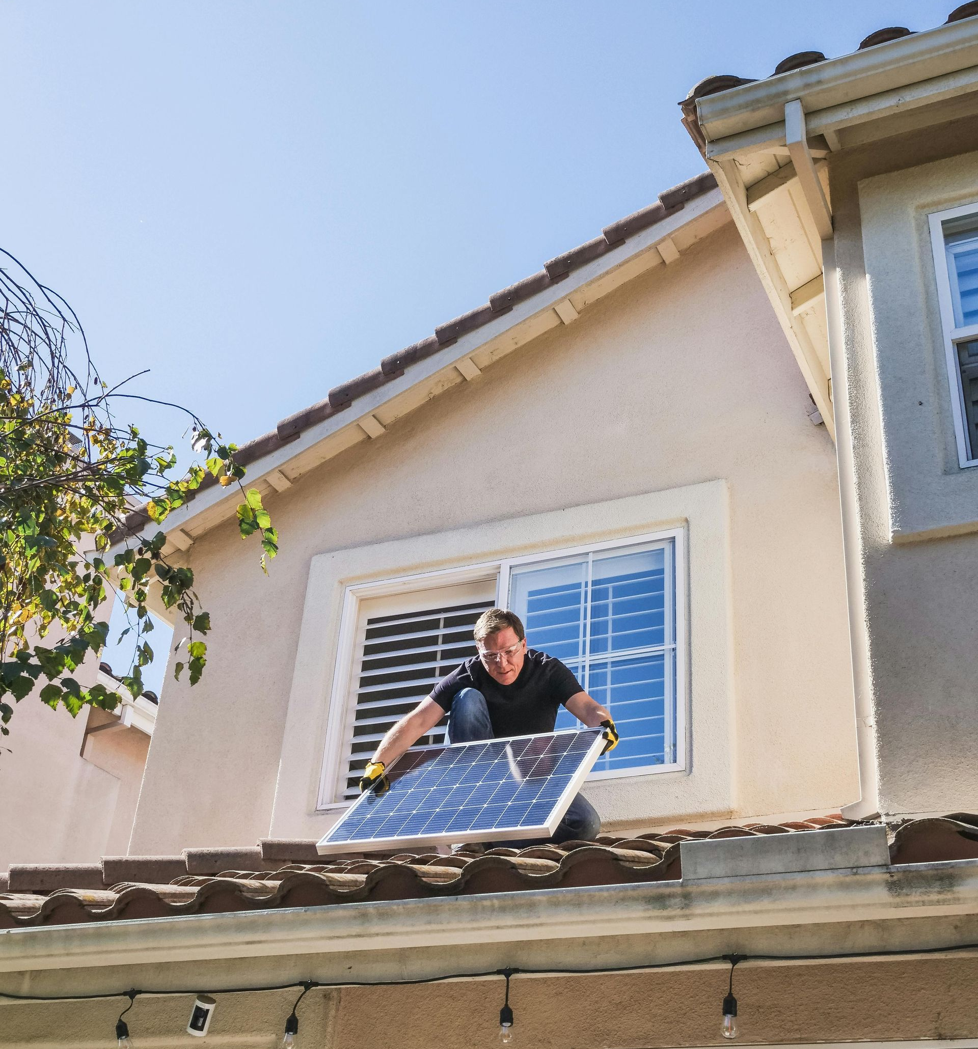 Man installing a solar panel on a rooftop against a clear sky.