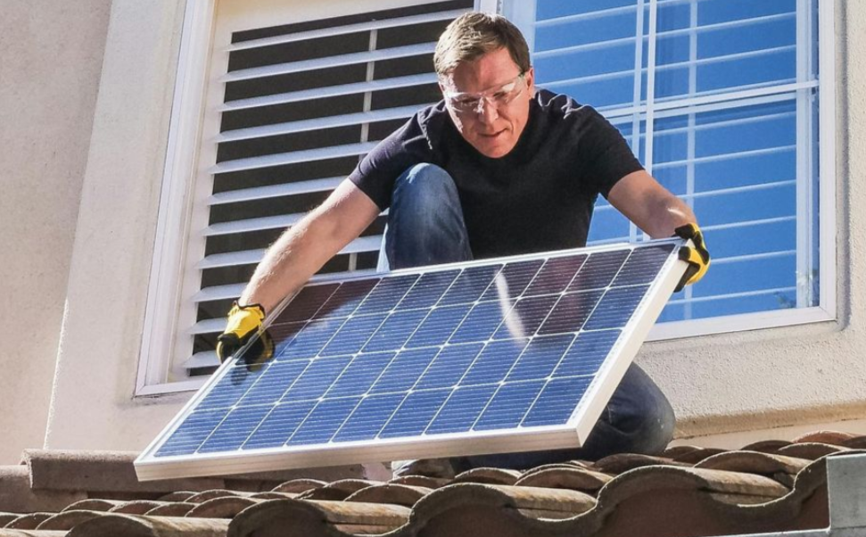 Man in safety glasses installs a solar panel on a rooftop.