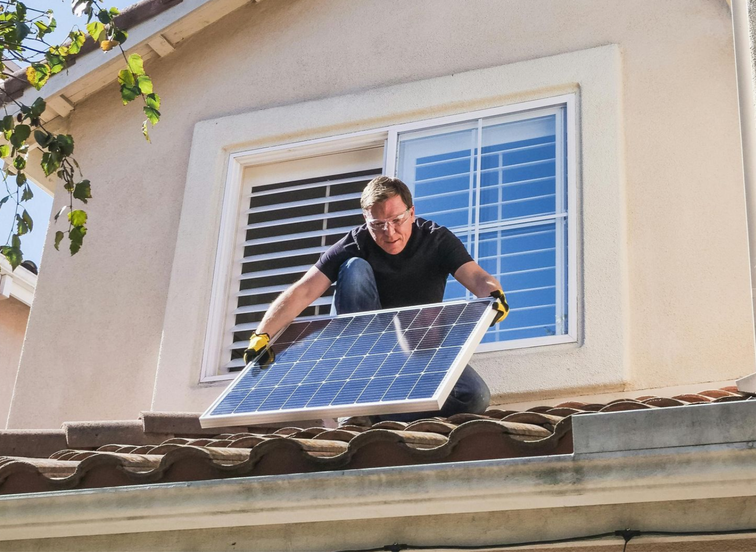 Man installing solar panel on a tiled roof near a window.