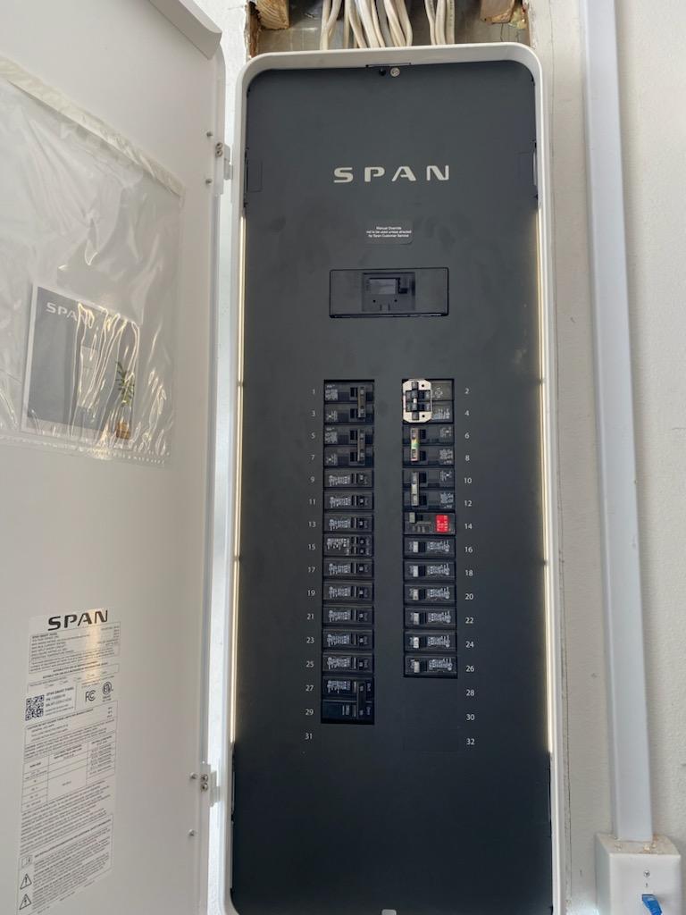 A gray Span smart electrical panel with circuit breakers, door open, mounted on a wall.