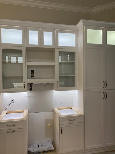 White kitchen cabinets with glass-fronted upper cabinets. Under-cabinet lighting illuminates the space.