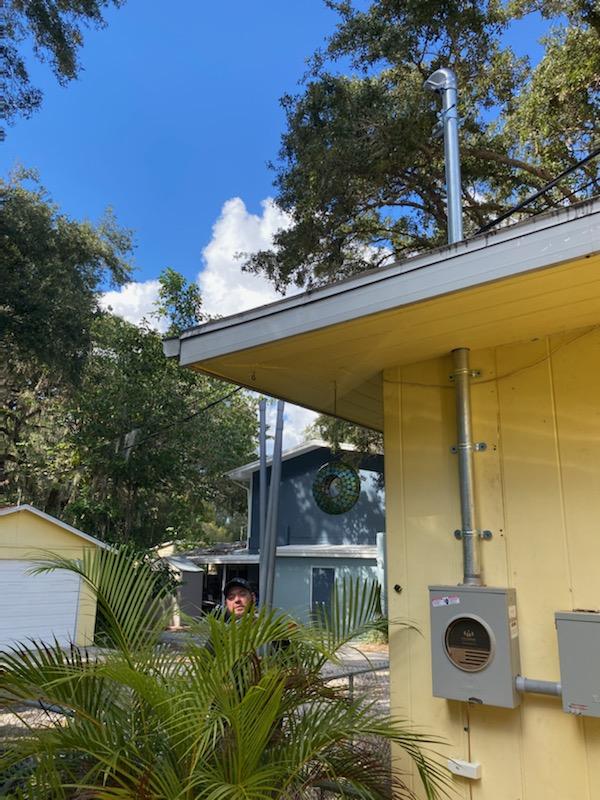 Yellow house with metal pipe extending to the sky, person hiding behind plant.