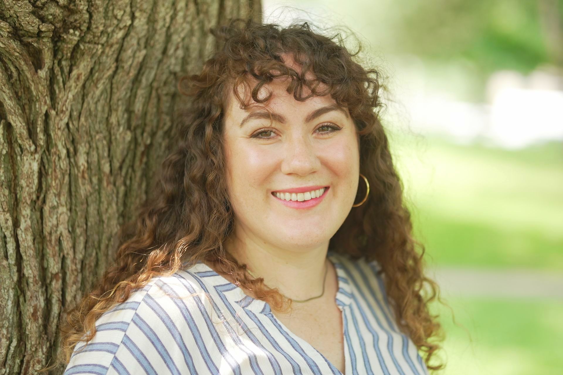 A woman posing by a tree trunk smiling in a professional manner in nature