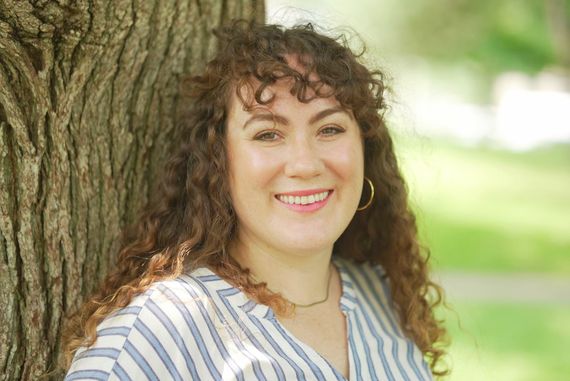 A woman posing by a tree trunk smiling in a professional manner in nature