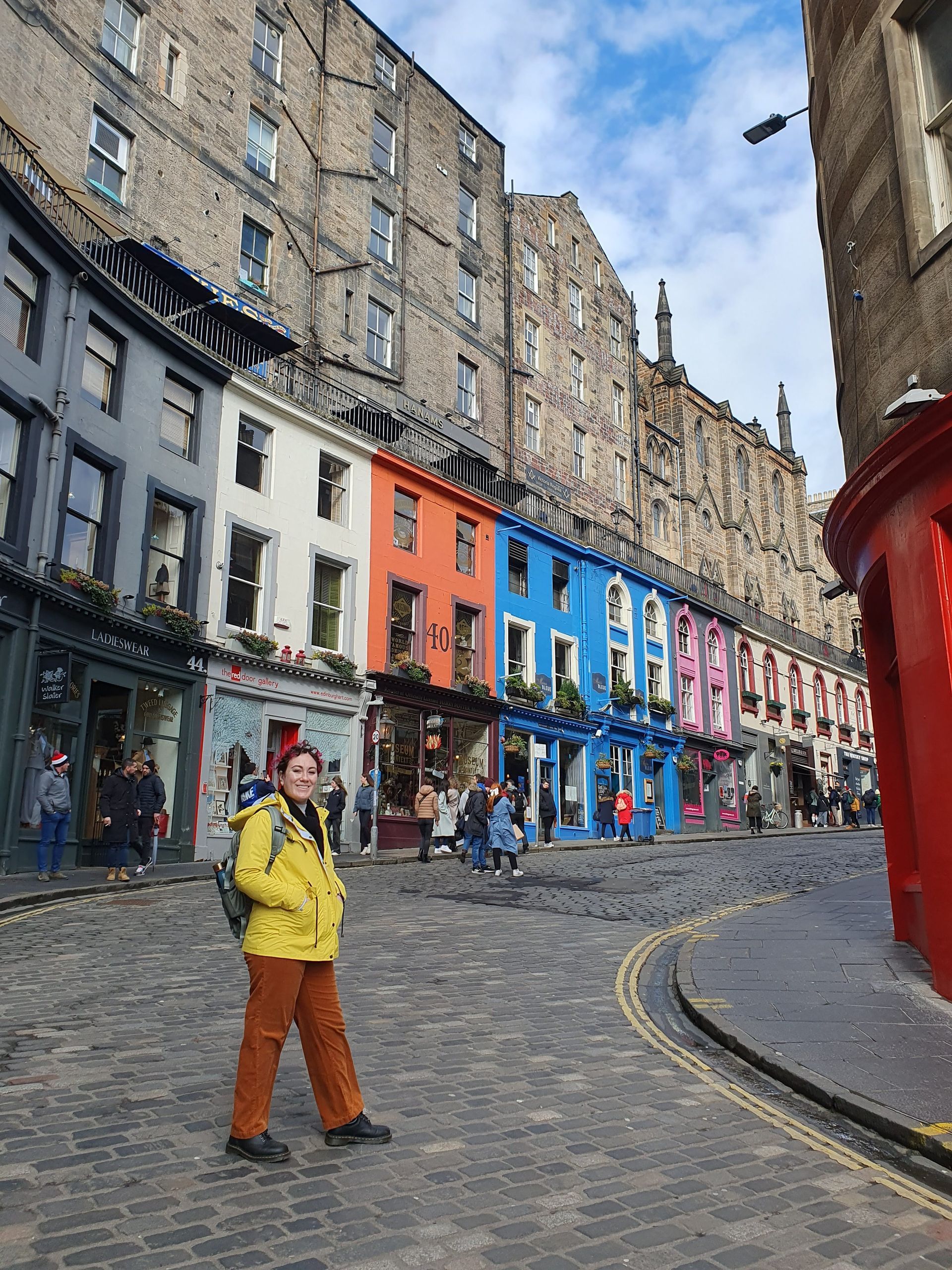 A person is walking down a cobblestone street in front of a row of colorful buildings.