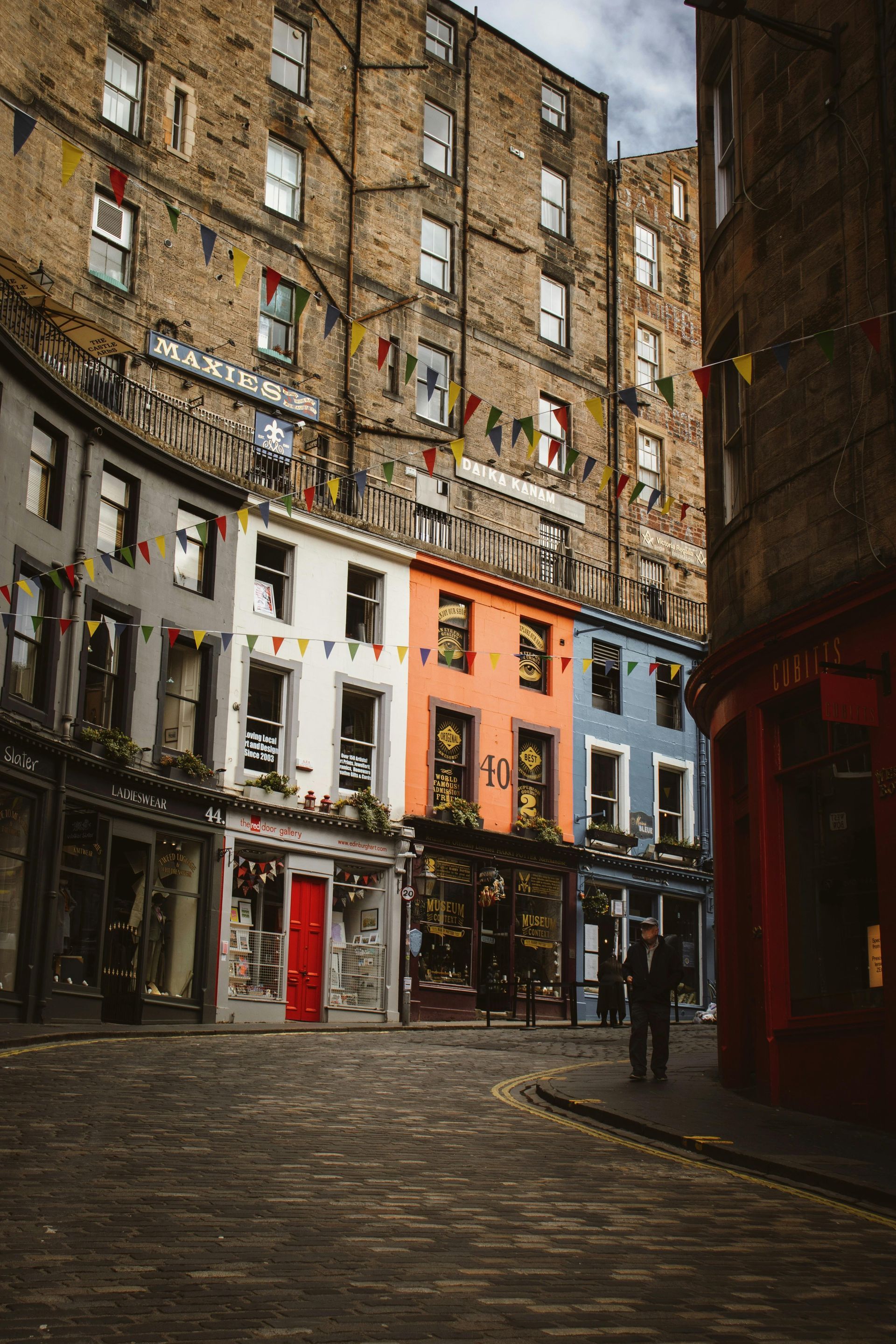 A man is walking down a cobblestone street between two tall buildings.