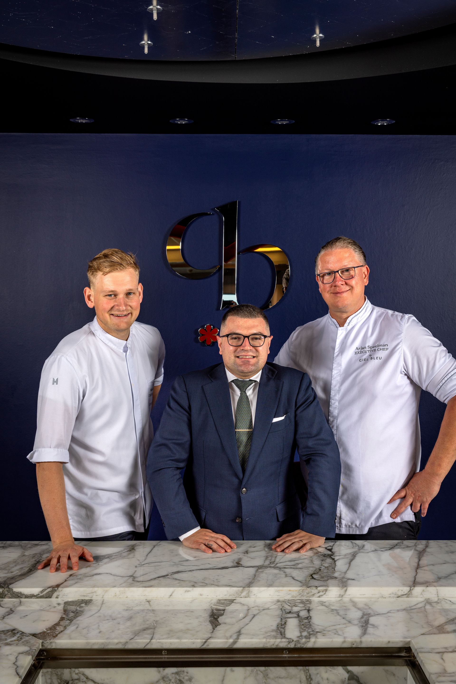 Three people posing: Francesco Simonelli, Arjan Speelman, and Mike Klassen in front of a marble counter and a dark blue wall.