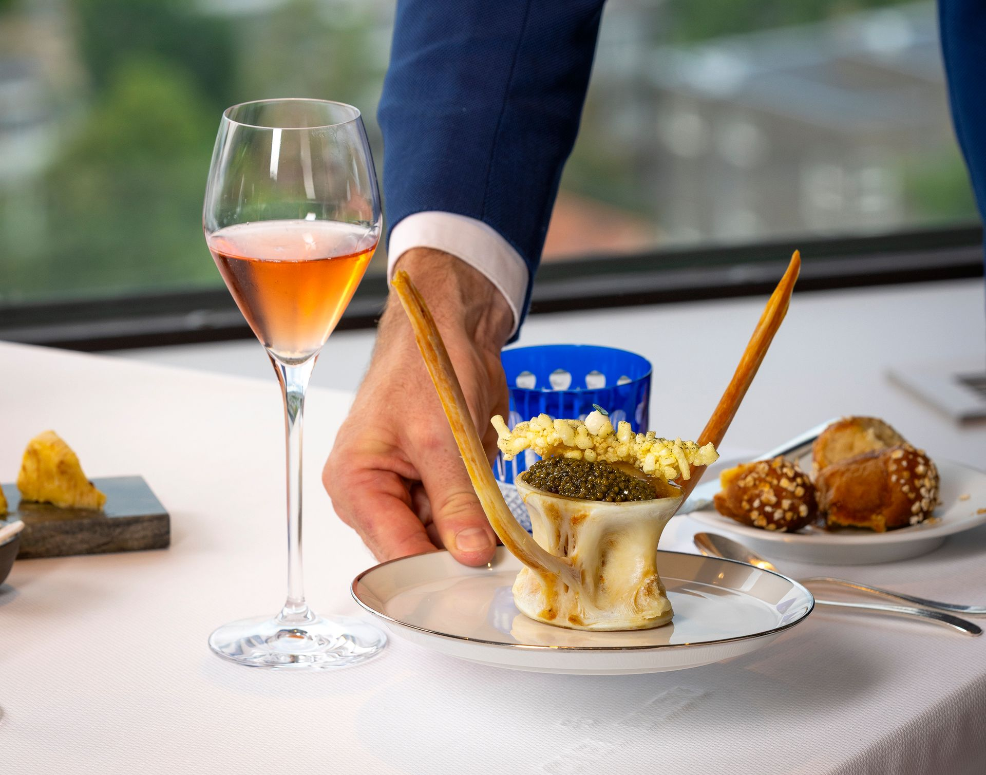 Een ober presenteert een voorgerecht bestaande uit kaviaar, stokbrood en een glas roséwijn.