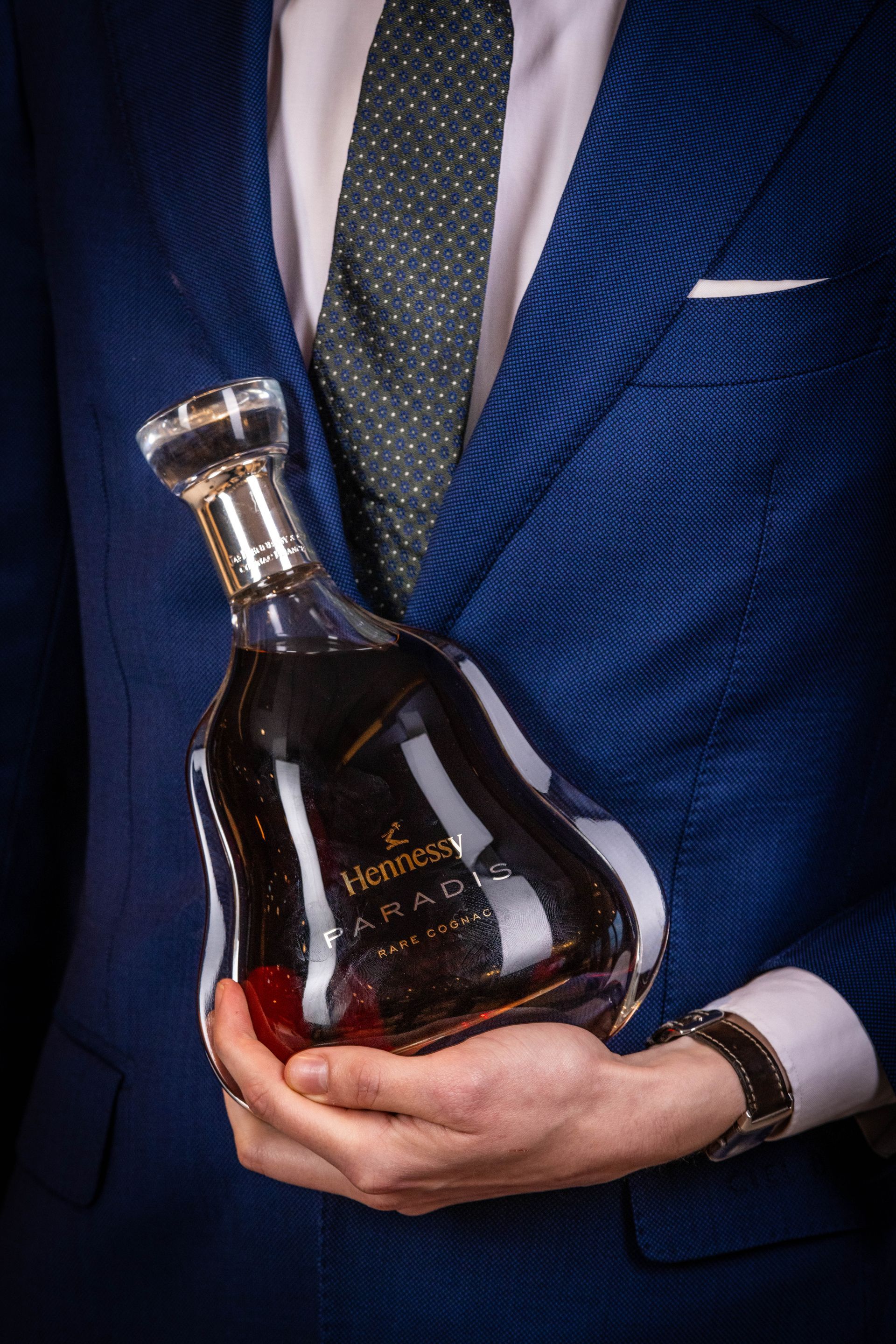 A man in a suit and tie is holding a bottle of cognac.