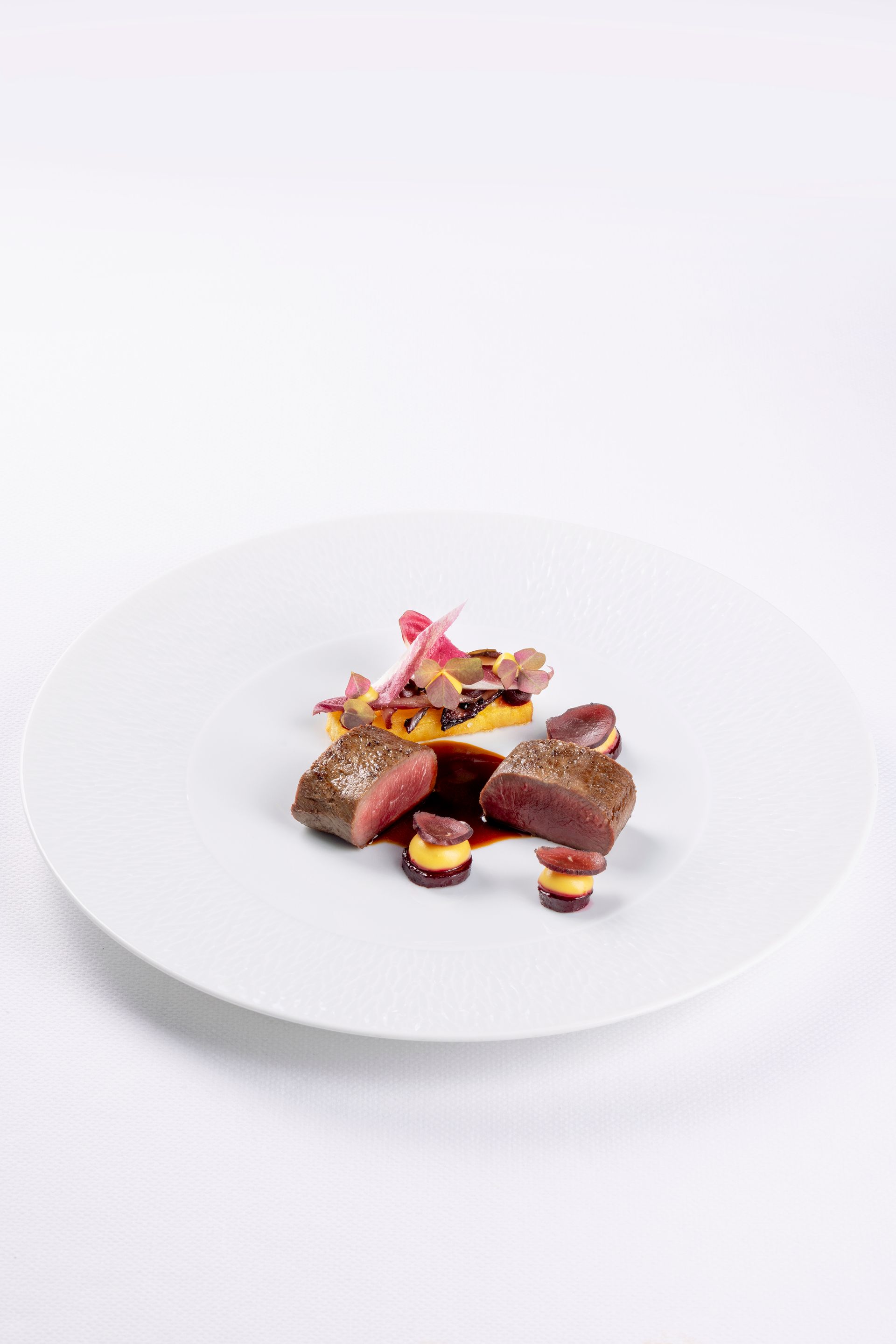 A white plate topped with meat and vegetables on a white background.