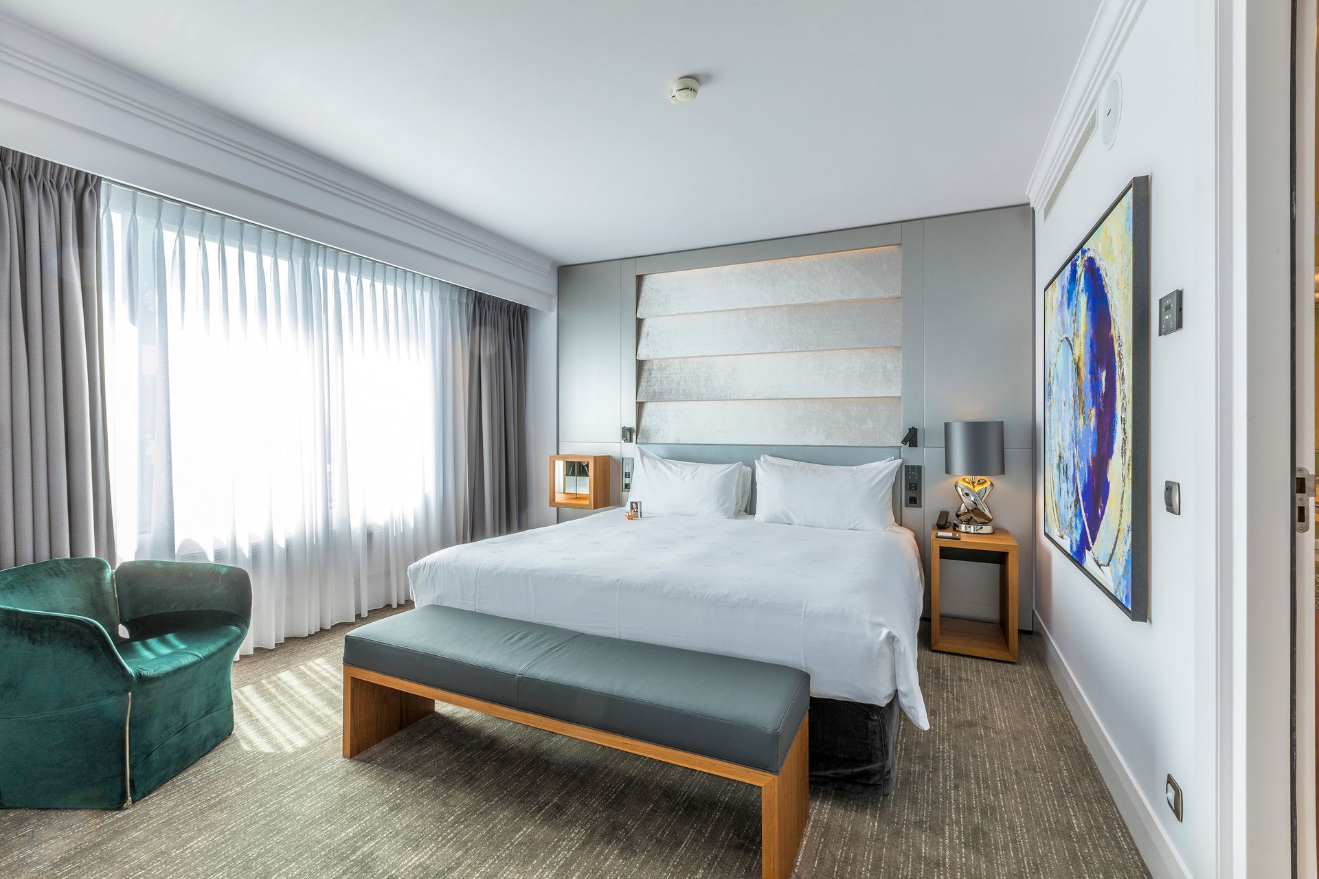 A hotel room with a king size bed and a bench.