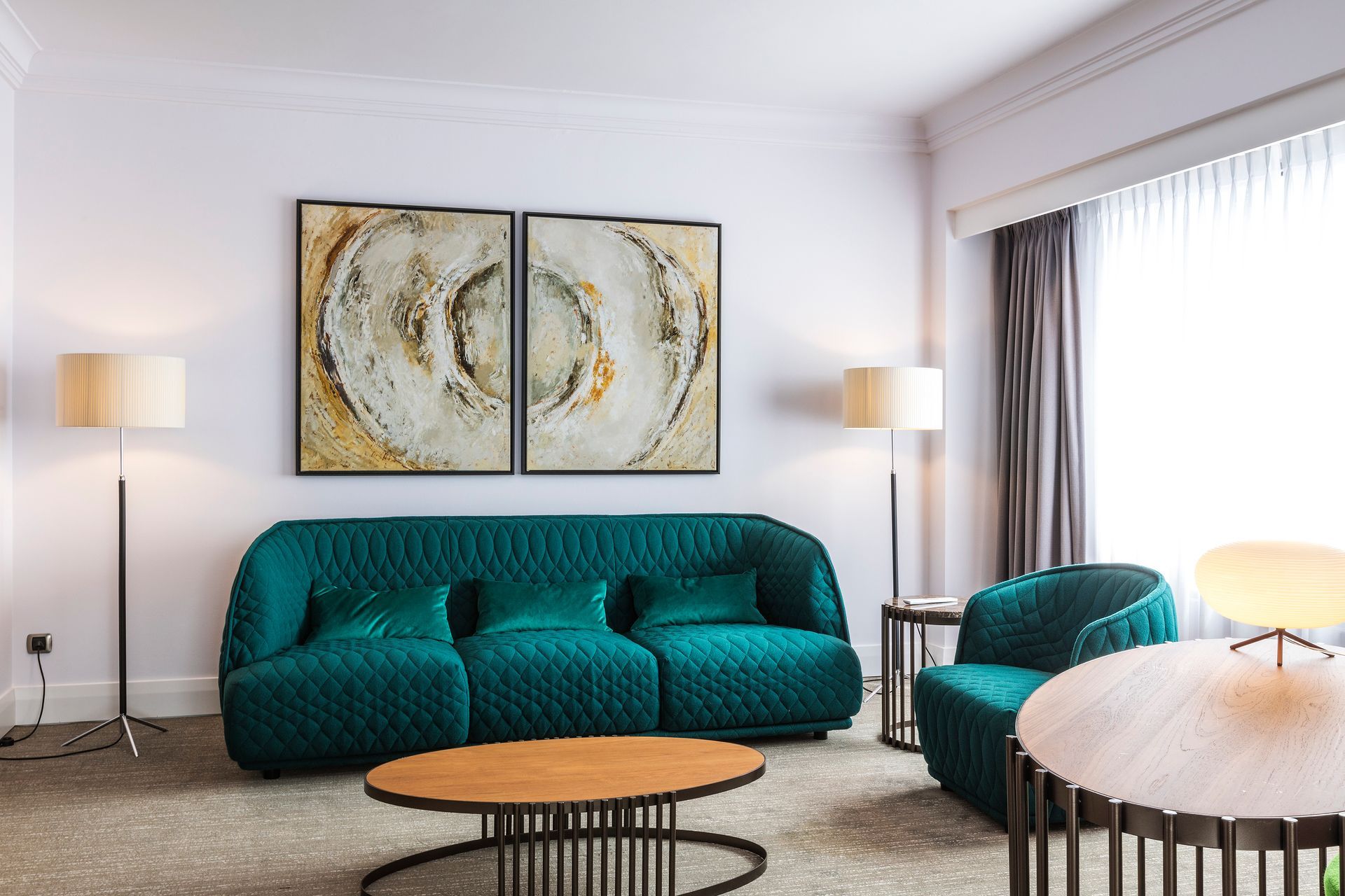 A living room with a green couch , chair , coffee table and two paintings on the wall.