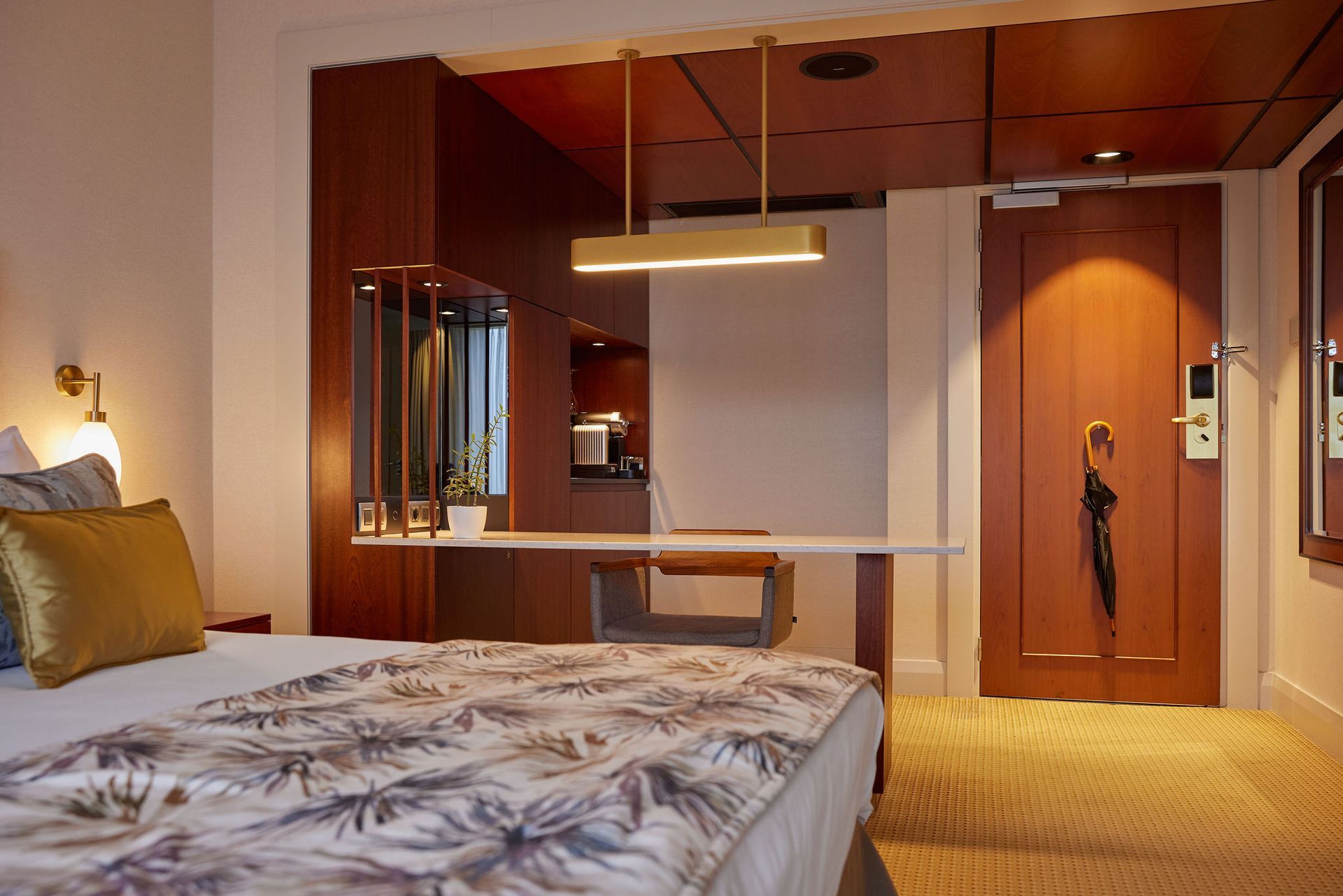 A hotel room with a bed , desk , mirror and door.