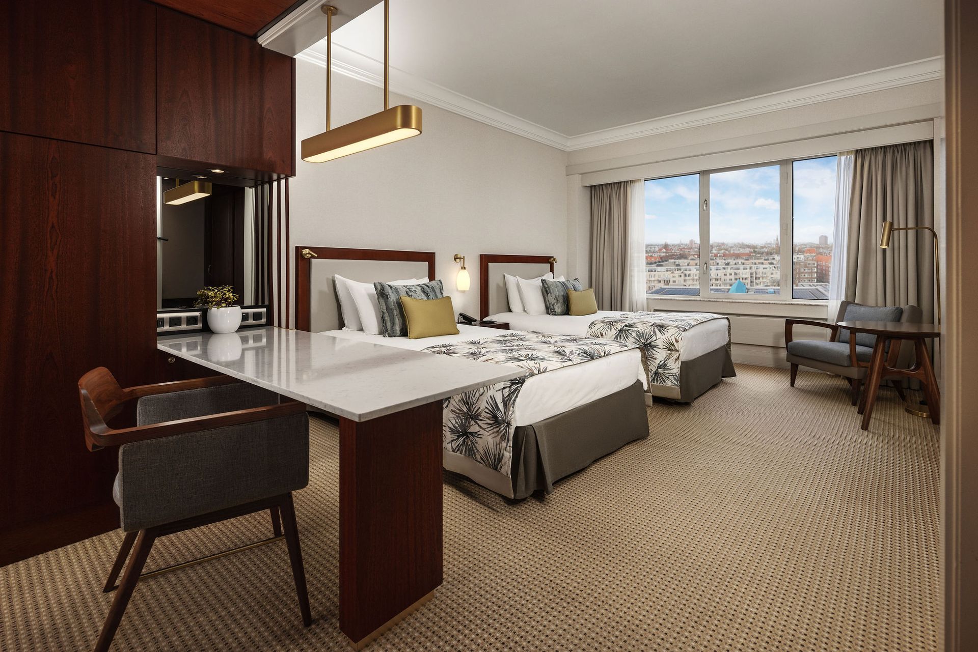 A hotel room with two beds , a desk , chairs and a large window.